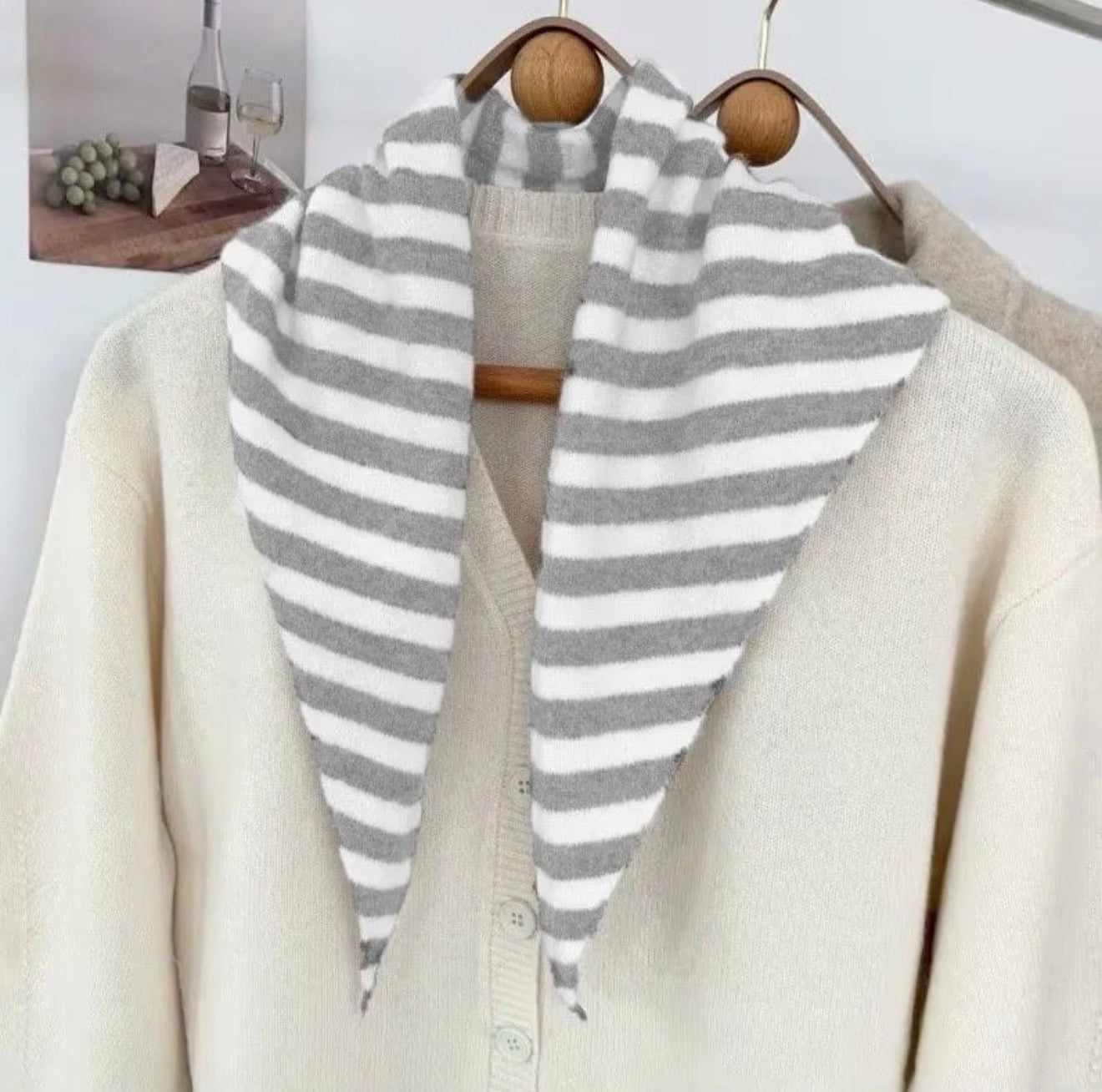 Grey and crean striped scarf draped over a cream-colored coat on a wooden hanger.