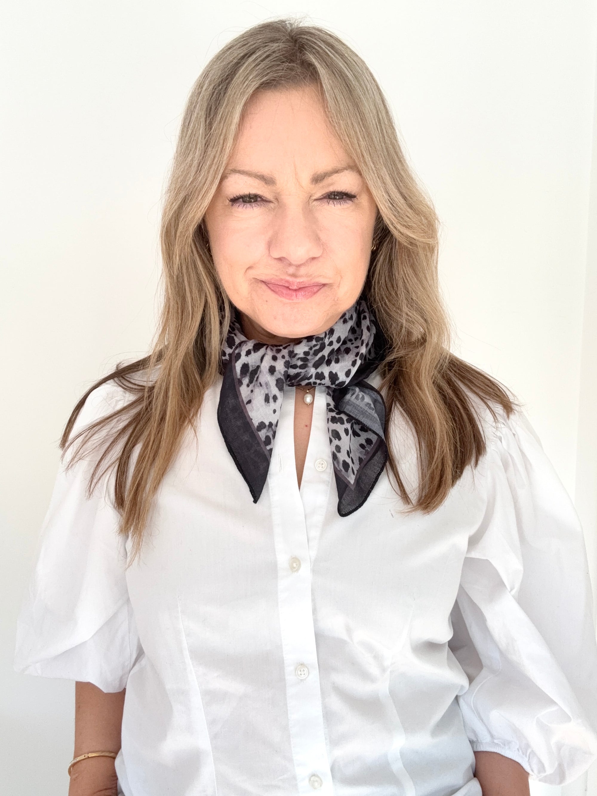 Woman wearing a white shirt and a grey animal print patterned scarf.