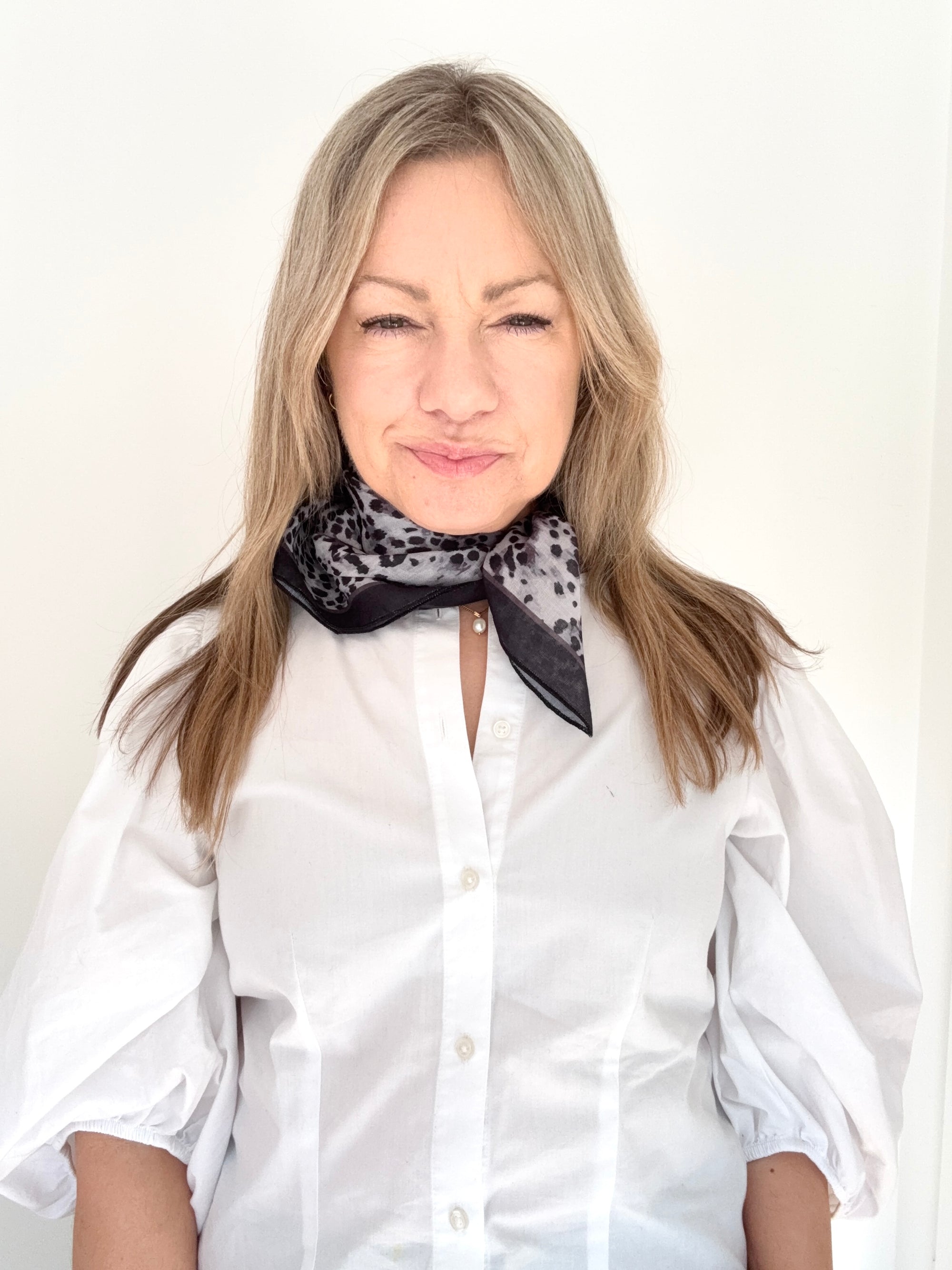 Woman wearing a white shirt and a grey animal print patterned scarf.