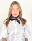 Woman wearing a white shirt and a grey animal print patterned scarf.