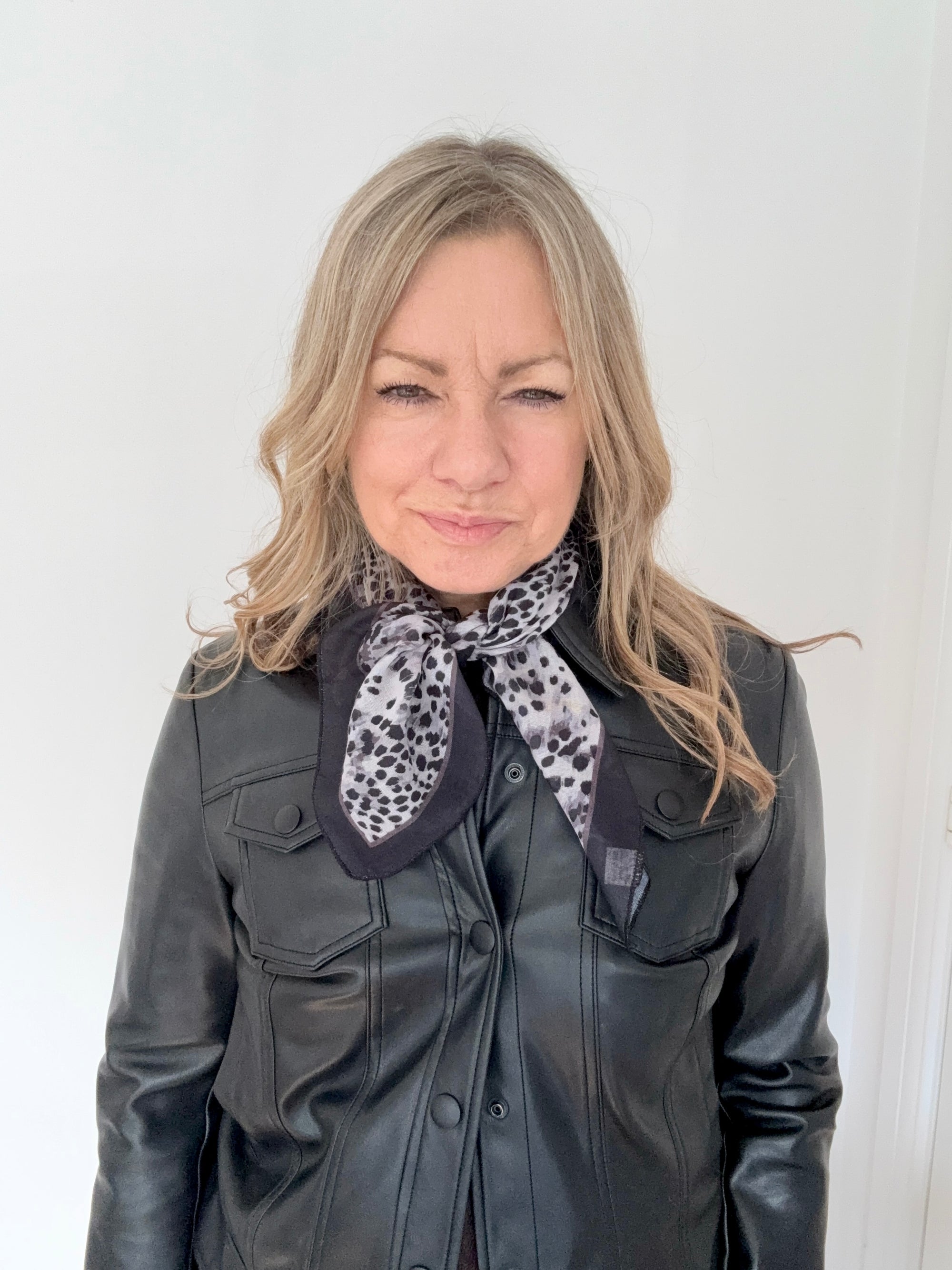 Woman wearing a black leather jacket with a grey animal print patterned scarf.