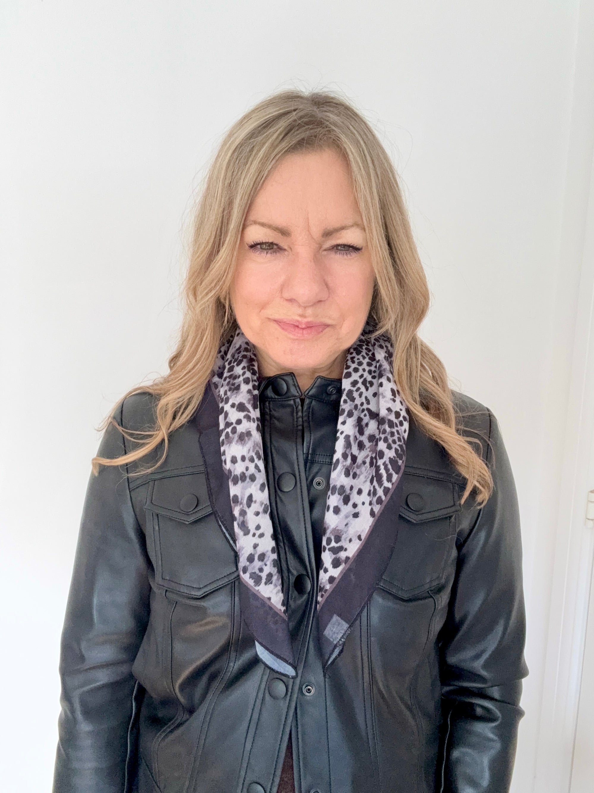 Woman wearing a black leather jacket with a grey animal print patterned scarf.