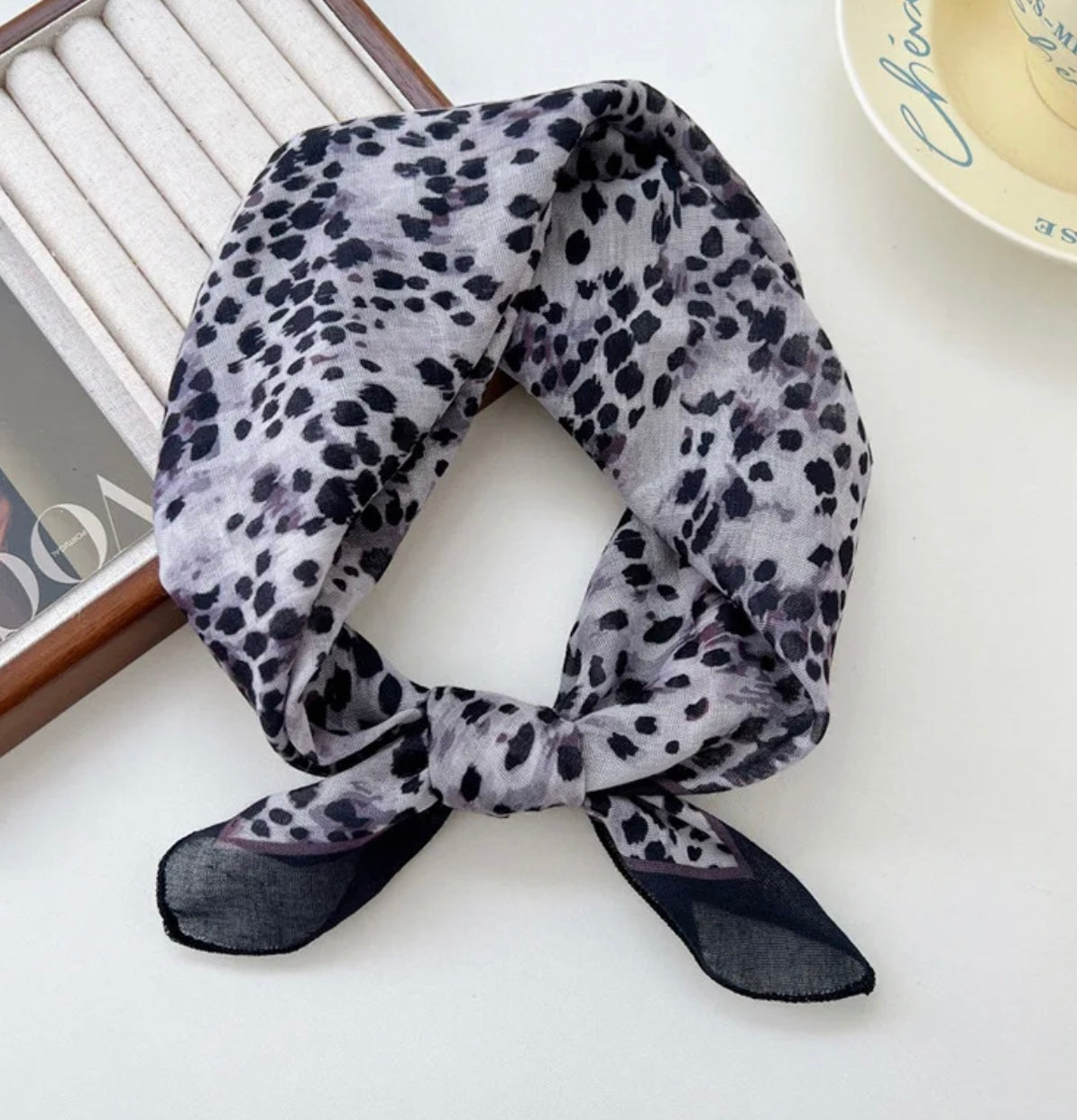 grey animal print square scarf on a white surface with a magazine in the background