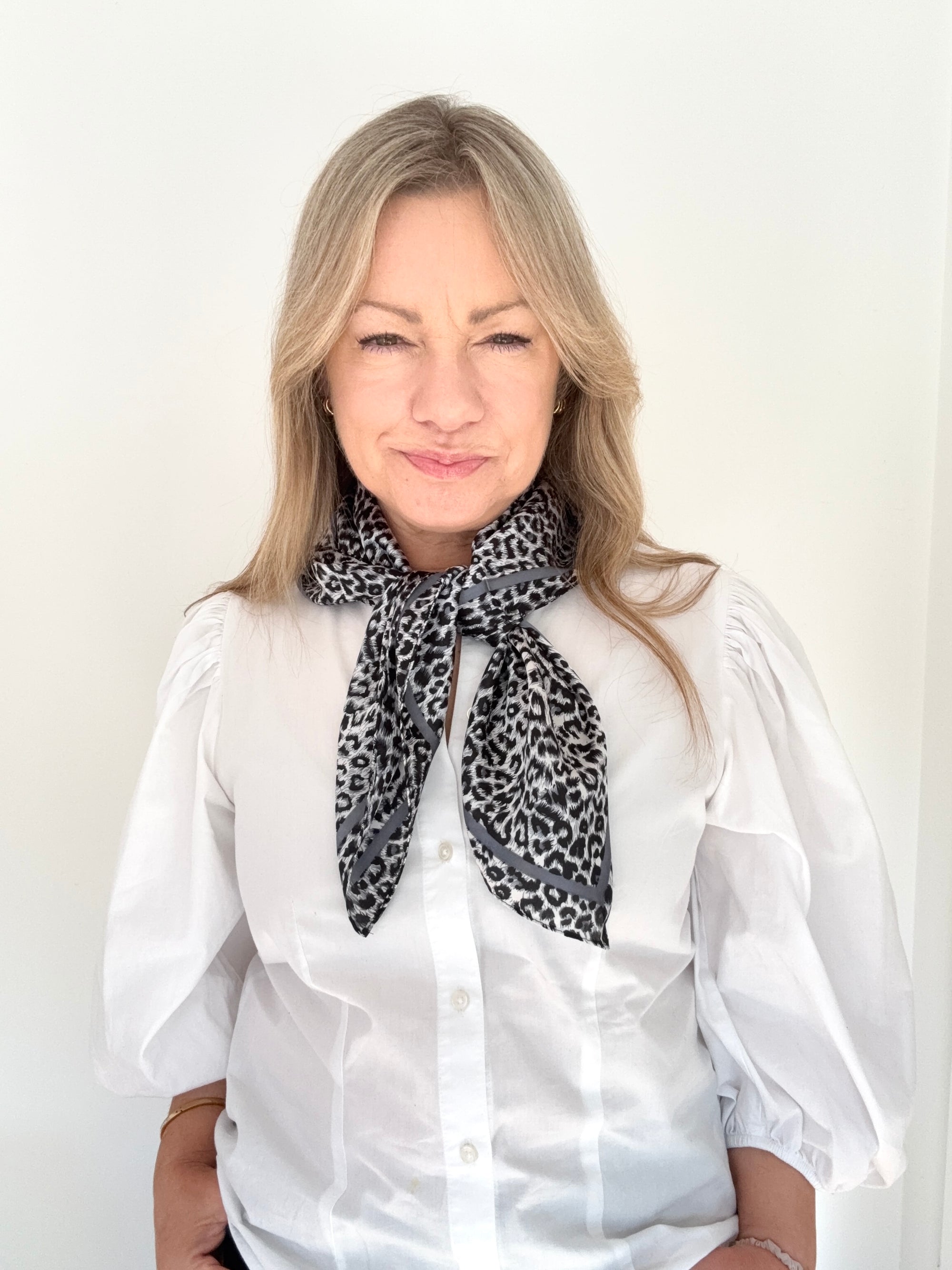 Woman wearing a white blouse and grey mix animal print scarf. 