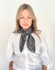 Woman wearing a white blouse and grey mix animal print scarf. 