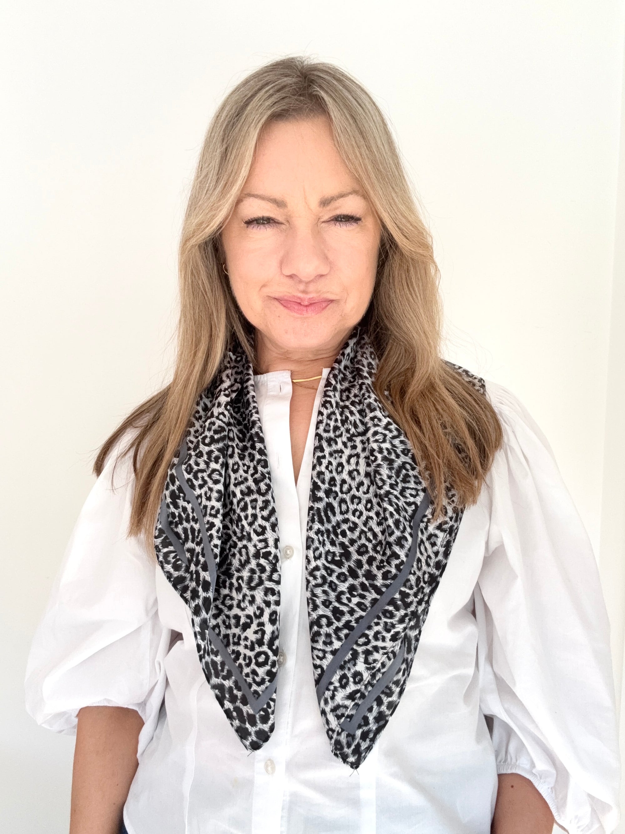 Woman wearing a white shirt and a grey mix animal print scarf.