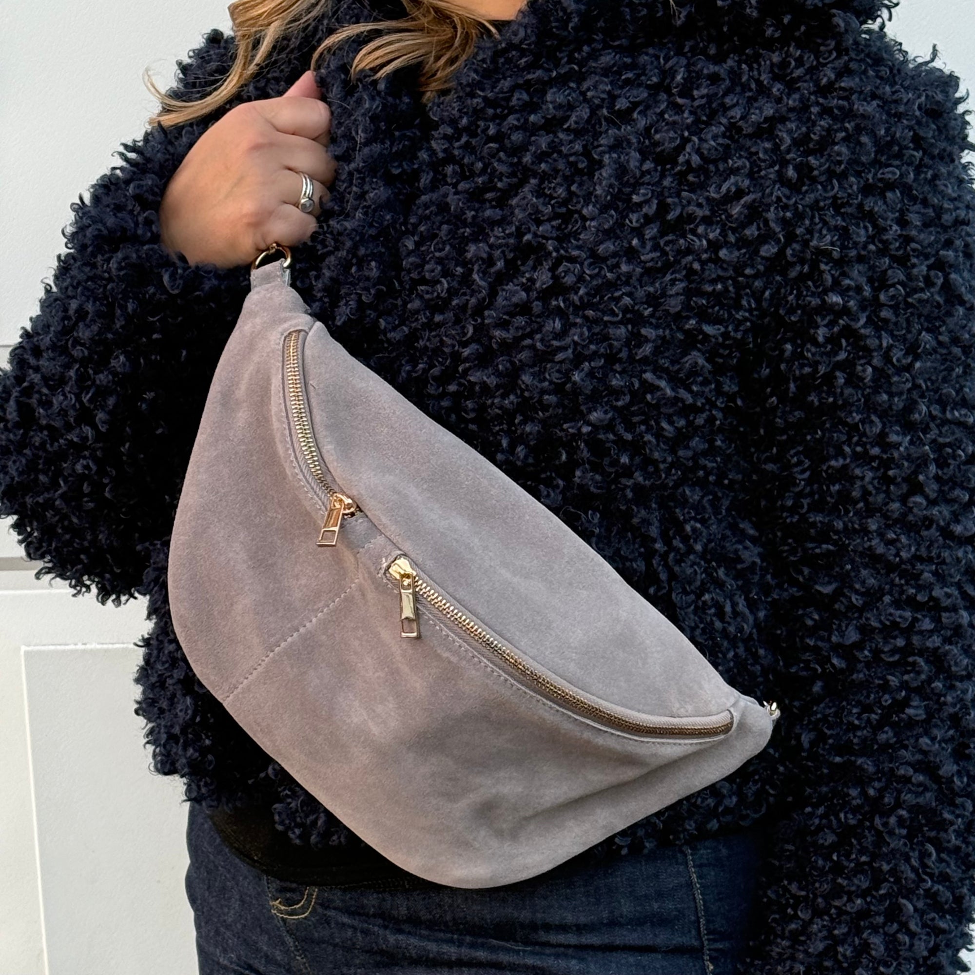 woman wearing a dark blue fuzzy jacket holding a large grey suede bag with gold zipper.