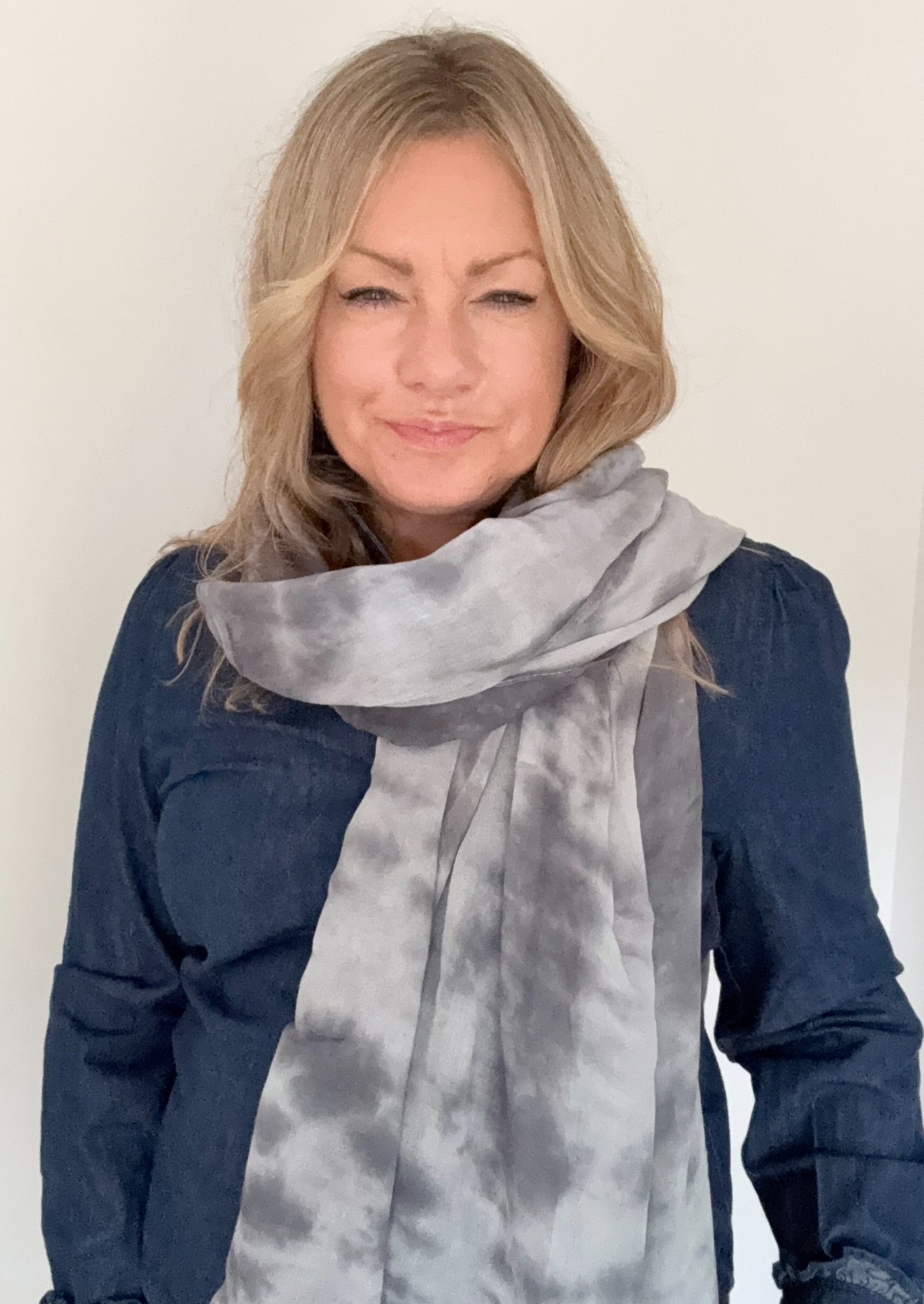 Woman wearing a grey tie-dye scarf with a plain background