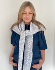 Woman wearing a blue top and a white and grey patterned scarf 
