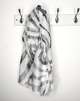 Black and white patterned scarf draped over a coat rack with three hooks on a white background
