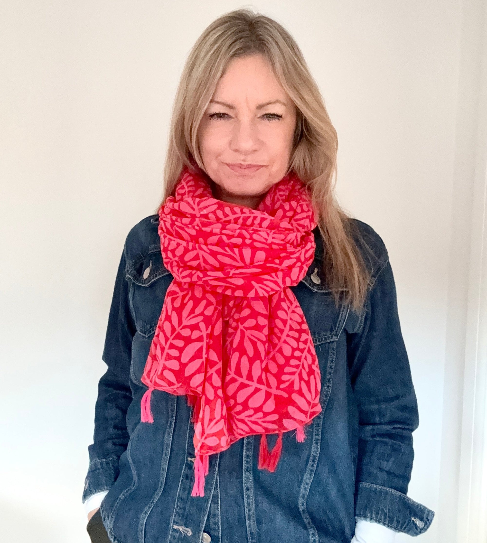 Woman wearing a red & pink cotton tassel scarf over a denim jacket 