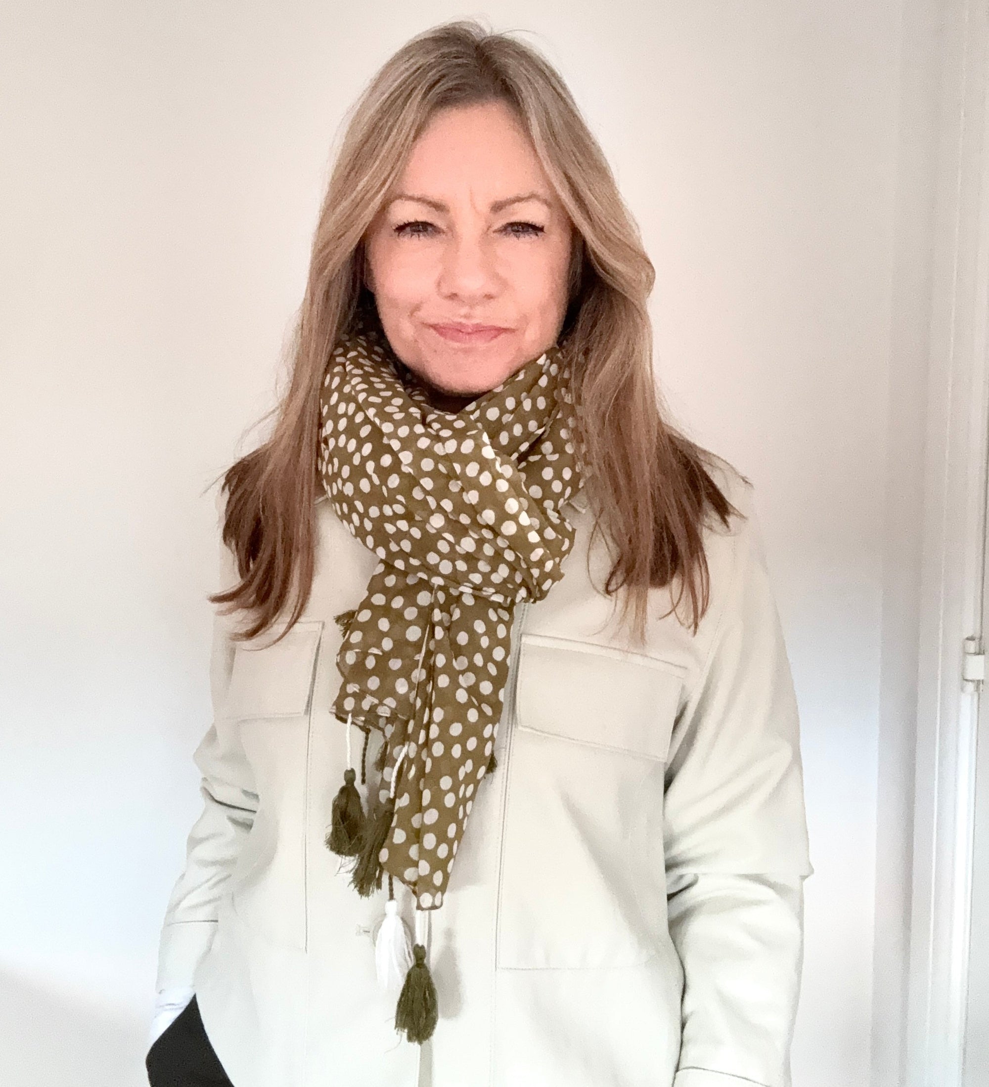 Woman wearing a khaki polka dot scarf with tassels against a white background