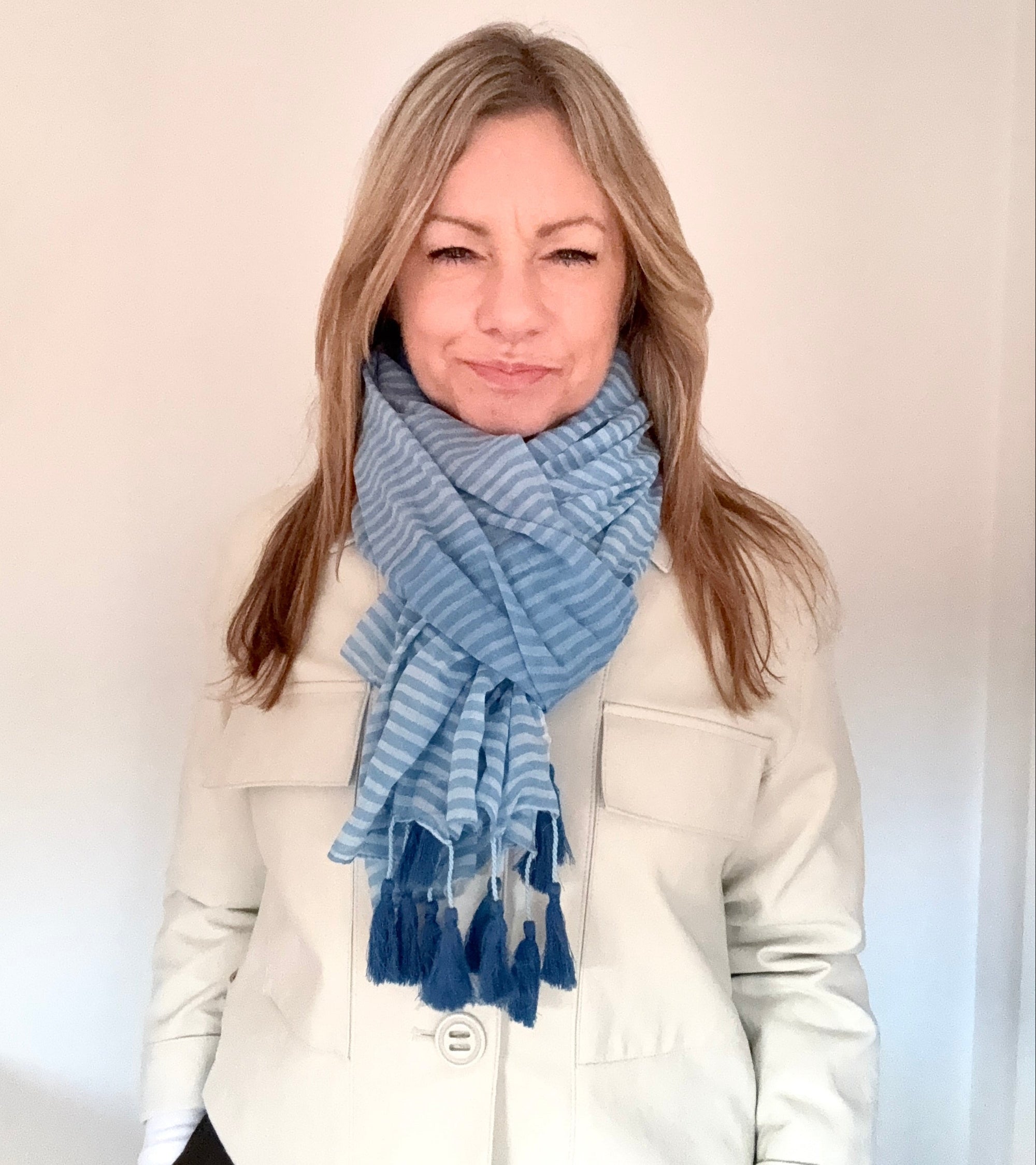 Woman wearing a blue striped cotton tassel scarf against a plain background