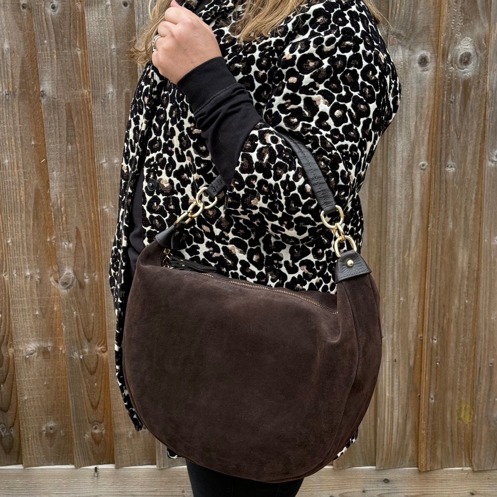 Person wearing a leopard print coat and holding a brown suede bag 