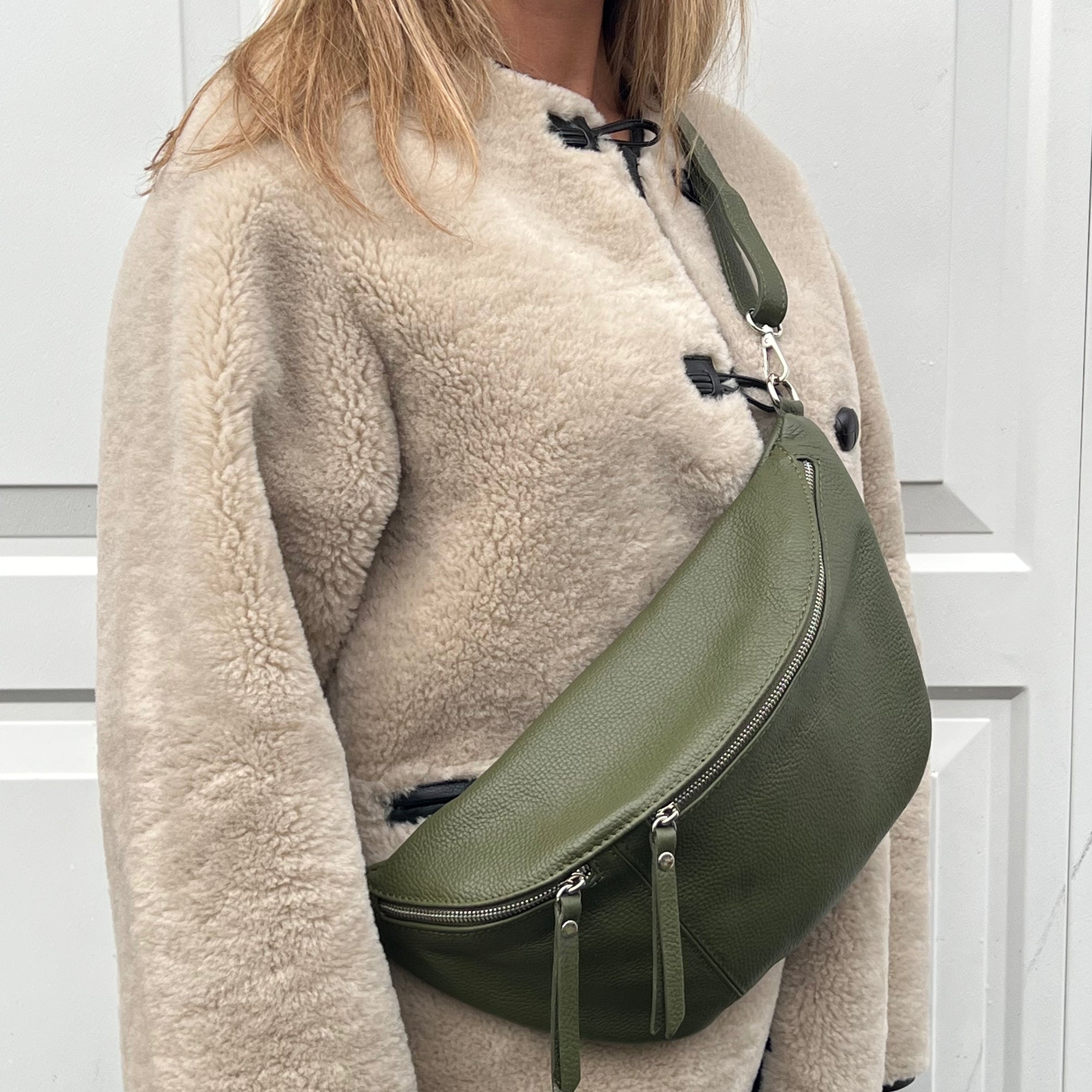 A woman wearing a khaki crossbody bum bag with silver accented hardware. 