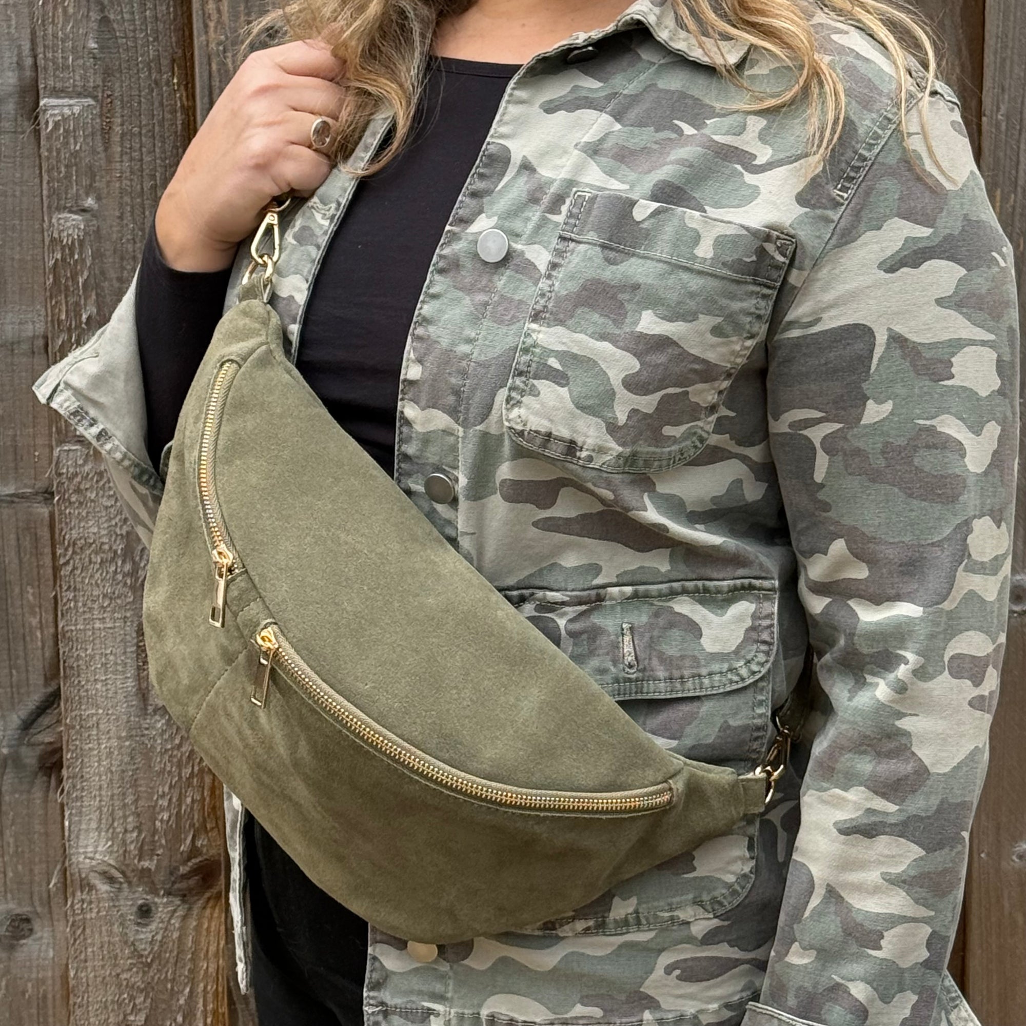 woman wearing a camouflage jacket holding an large suede khaki green crossbody bum bag 
