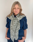 Woman wearing a khaki and white  leopard print scarf and blue top 