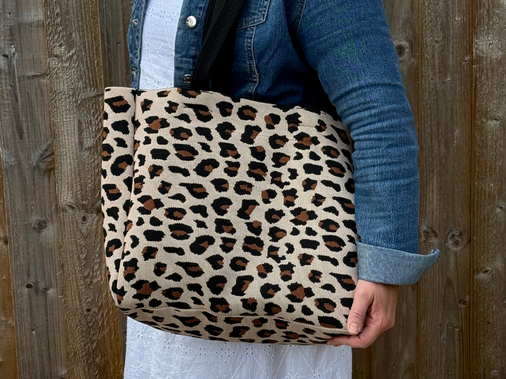 Person holding a leopard print bag against a wooden background