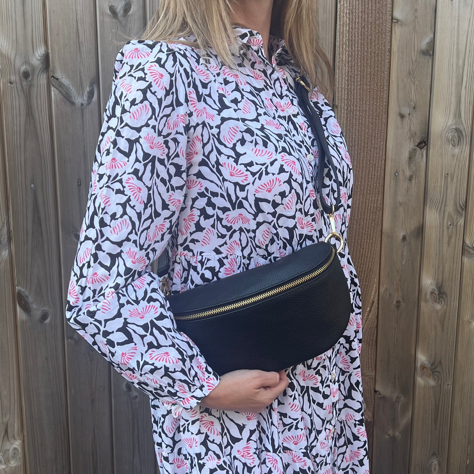 A woman wearing  a large black leather crossbody bag with an adjustable strap and gold hardware. 
