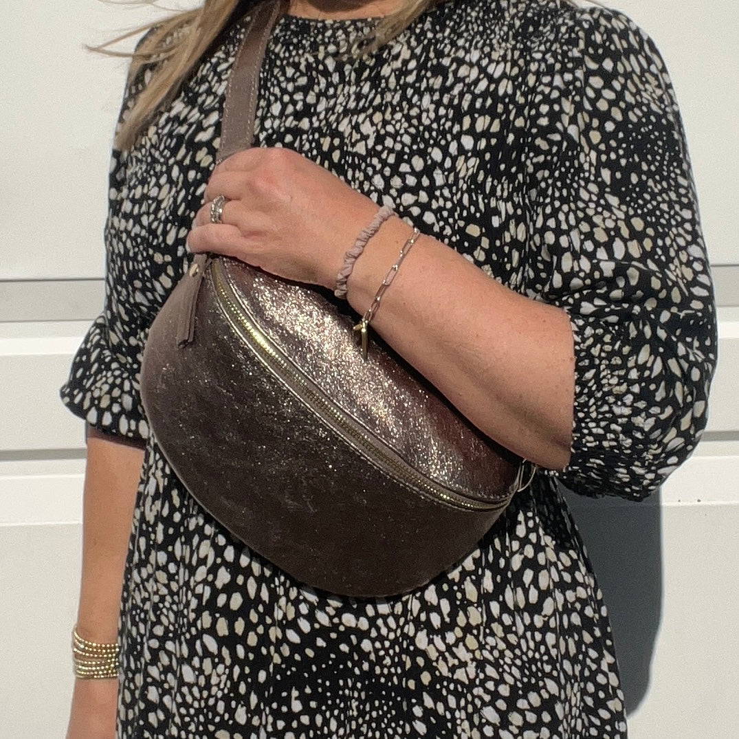A woman wearing a large bronze leather crossbody bag with a dotted pattern on the fabric and gold  hardware.