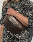 A woman wearing a large bronze leather crossbody bag with a dotted pattern on the fabric and gold  hardware.