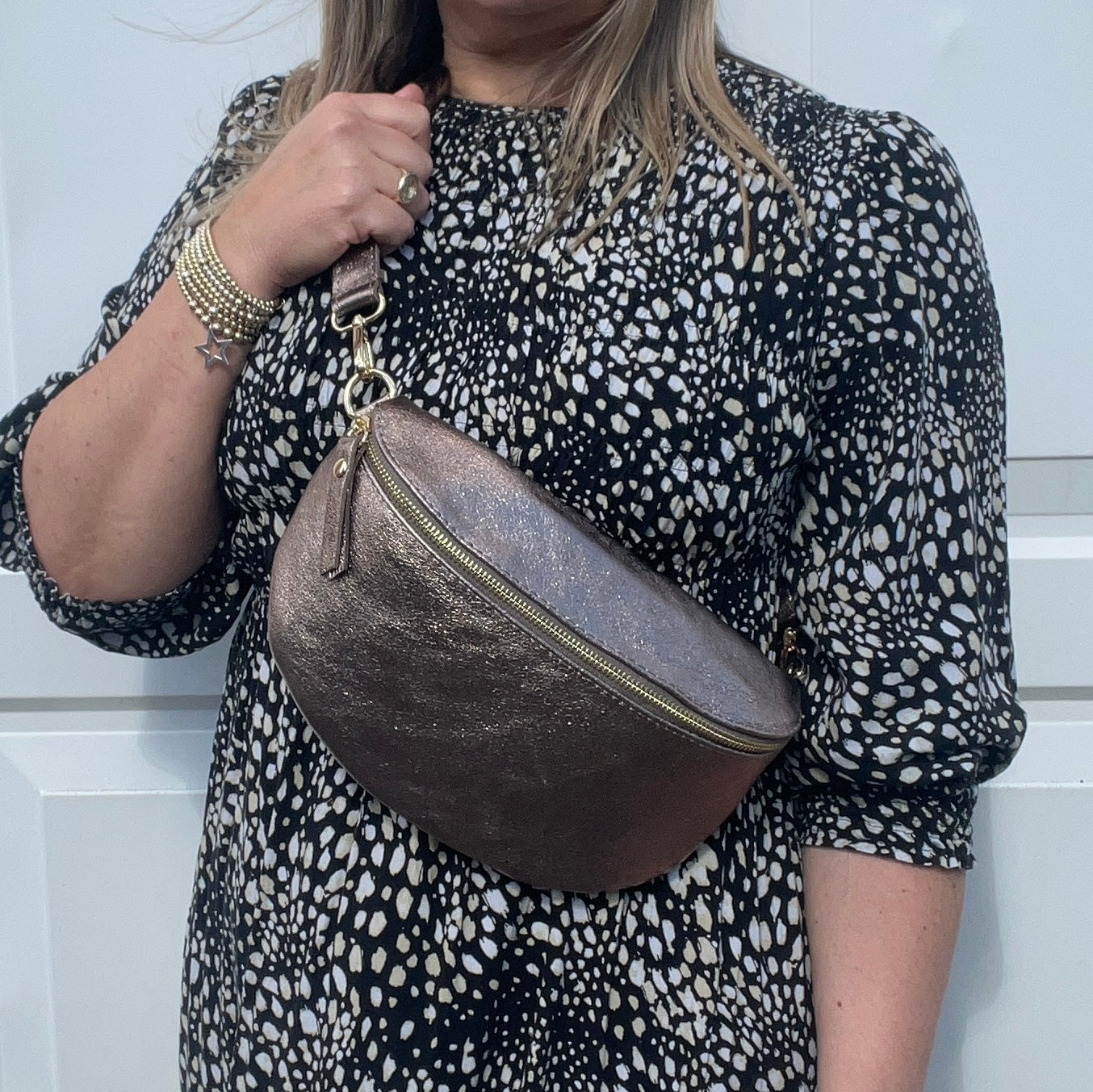 A woman wearing a large bronze leather crossbody bag with a dotted pattern on the fabric and gold  hardware.
