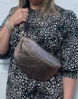 A woman wearing a large bronze leather crossbody bag with a dotted pattern on the fabric and gold  hardware.
