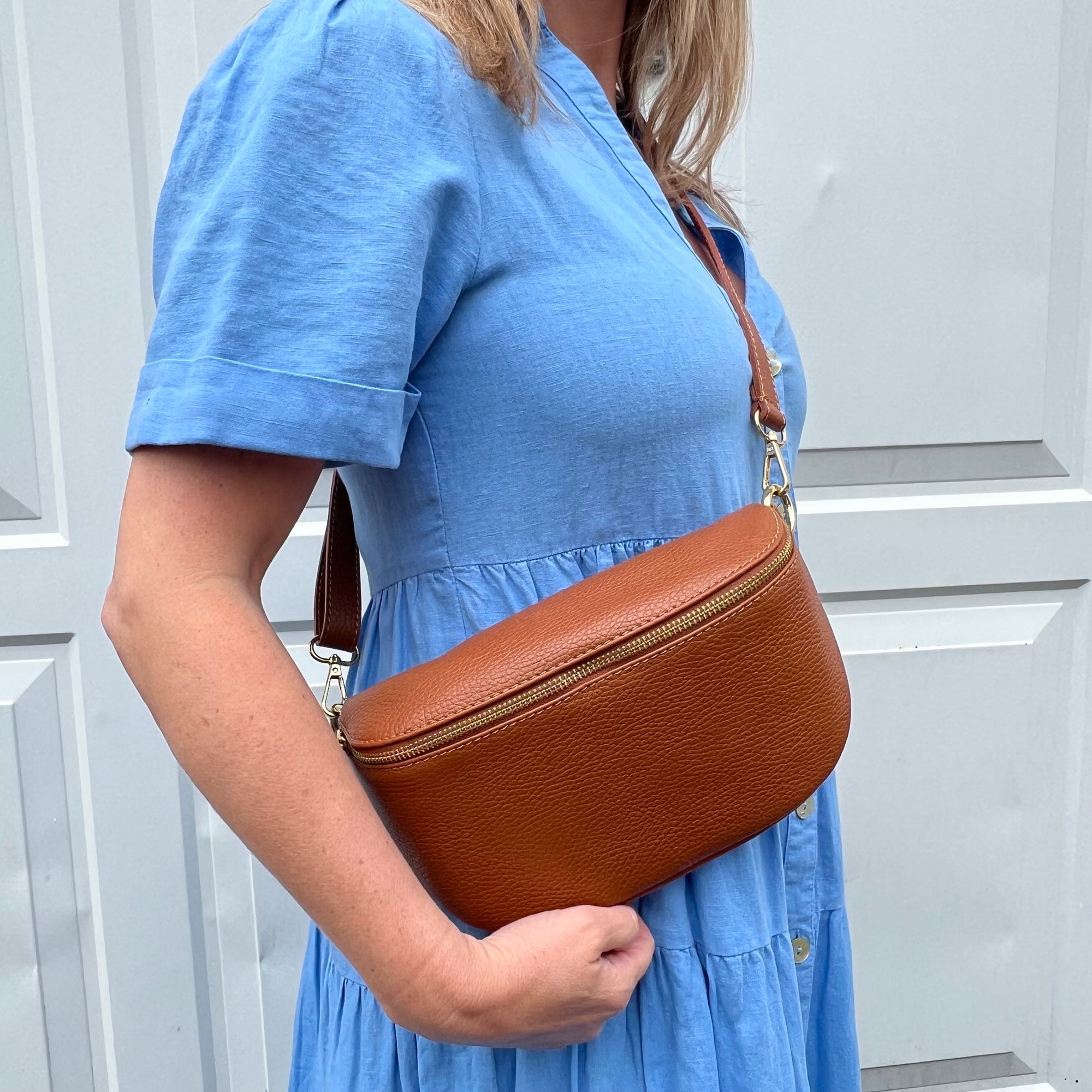 a woman wearing a large dark tan crossbody / waist bag with an adjustable strap and gold hardware.