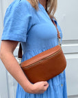 a woman wearing a large dark tan crossbody / waist bag with an adjustable strap and gold hardware.
