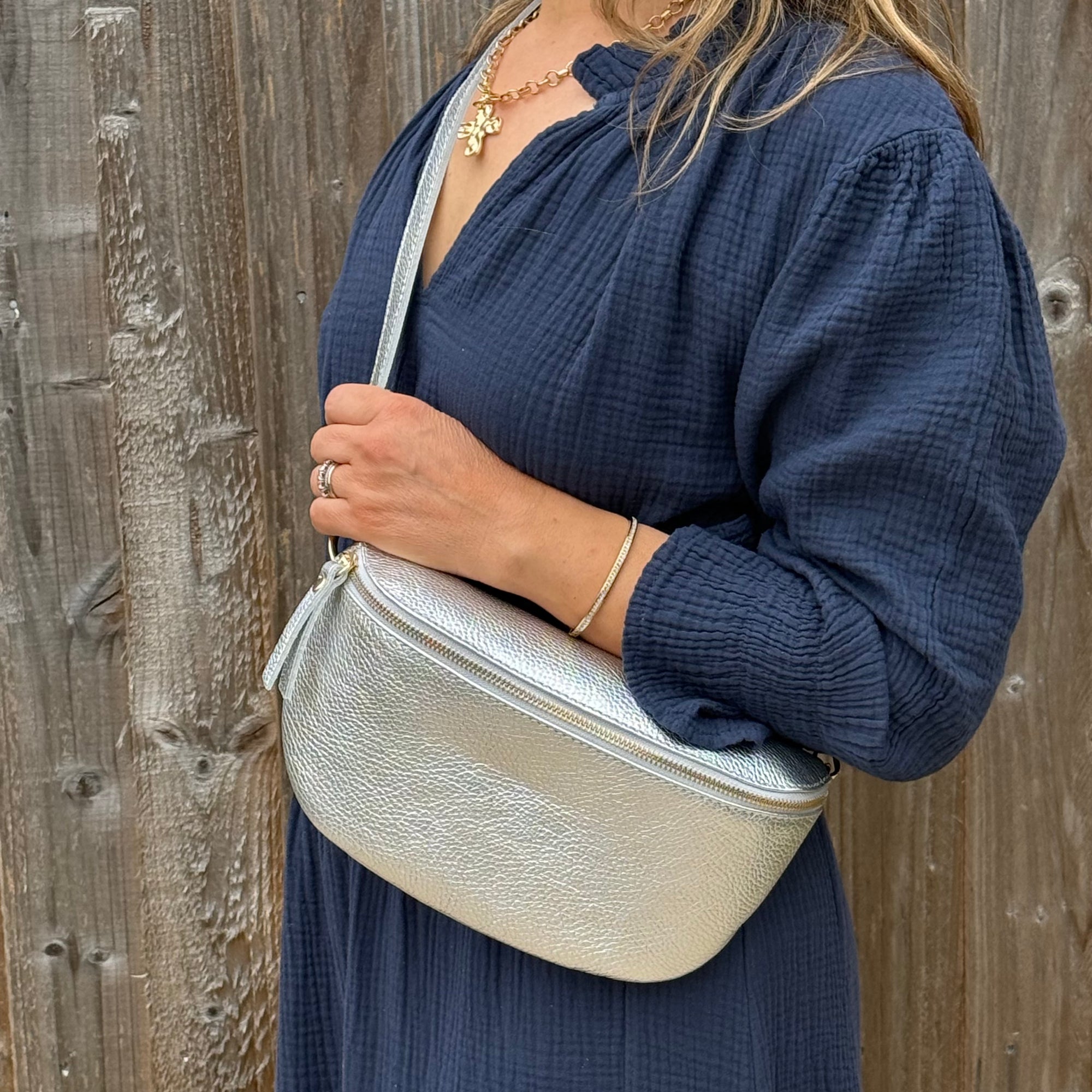 Woman wearing a navy dress, holding a silver crossbody bag against a wooden background.