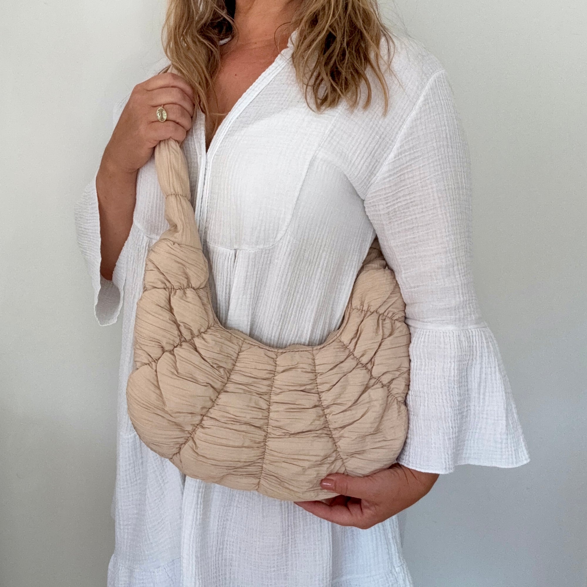Woman holding a beige croissant textured shoulder handbag 