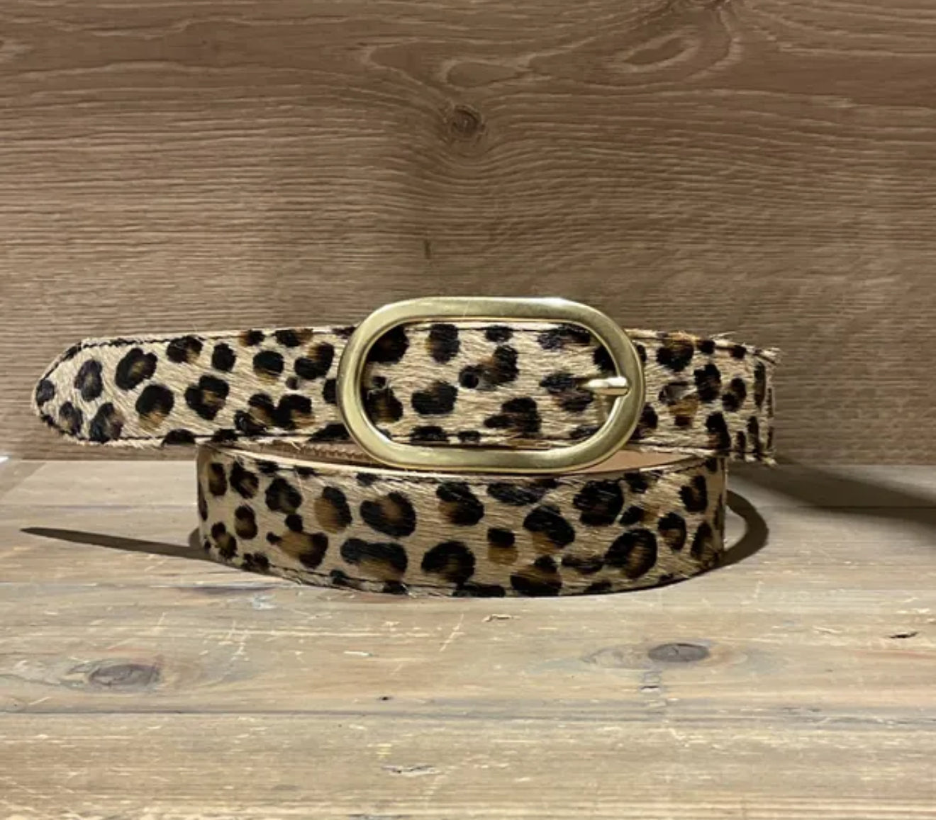 Leopard print belt with a gold buckle on a wooden surface