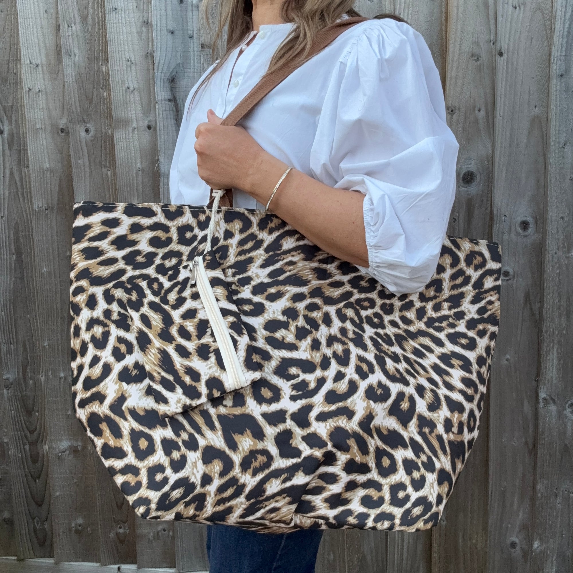 Woman wearing a white shirt, holding a leopard print tote bag .