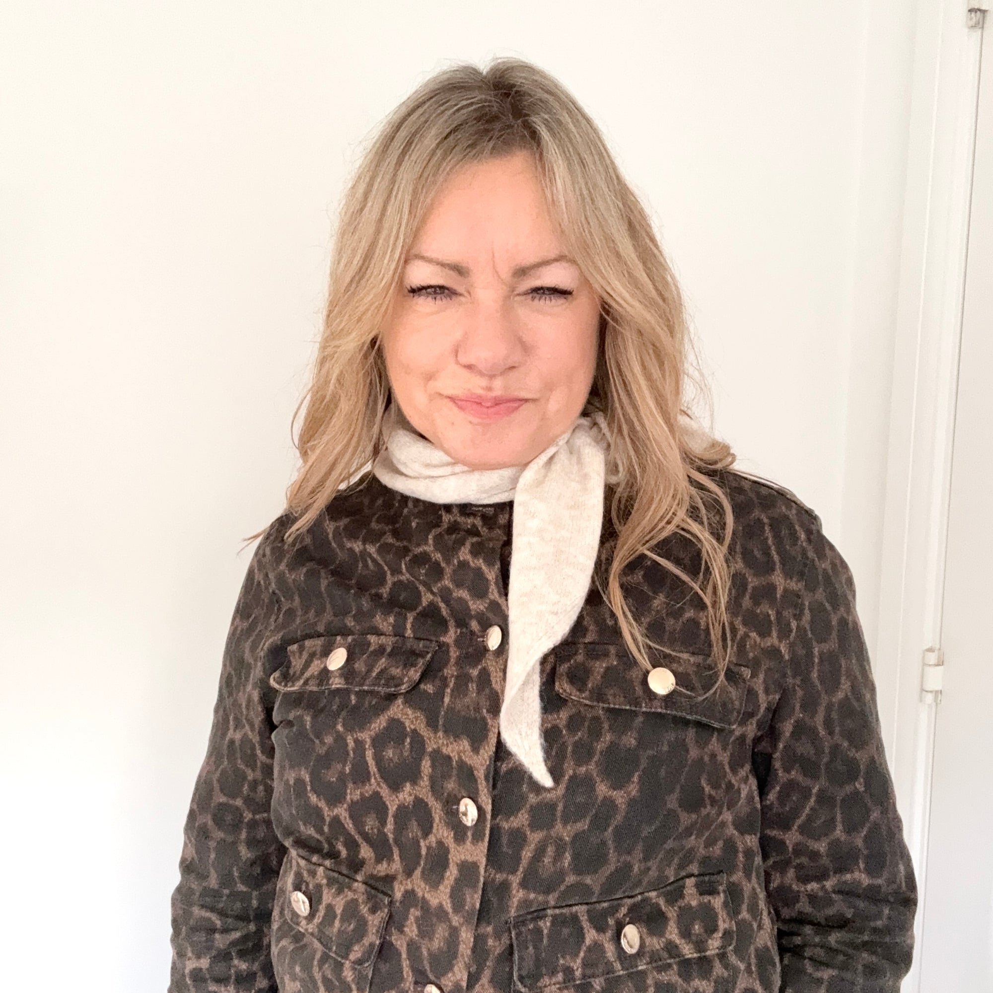 Woman wearing a leopard print jacket with a white scarf against a plain background