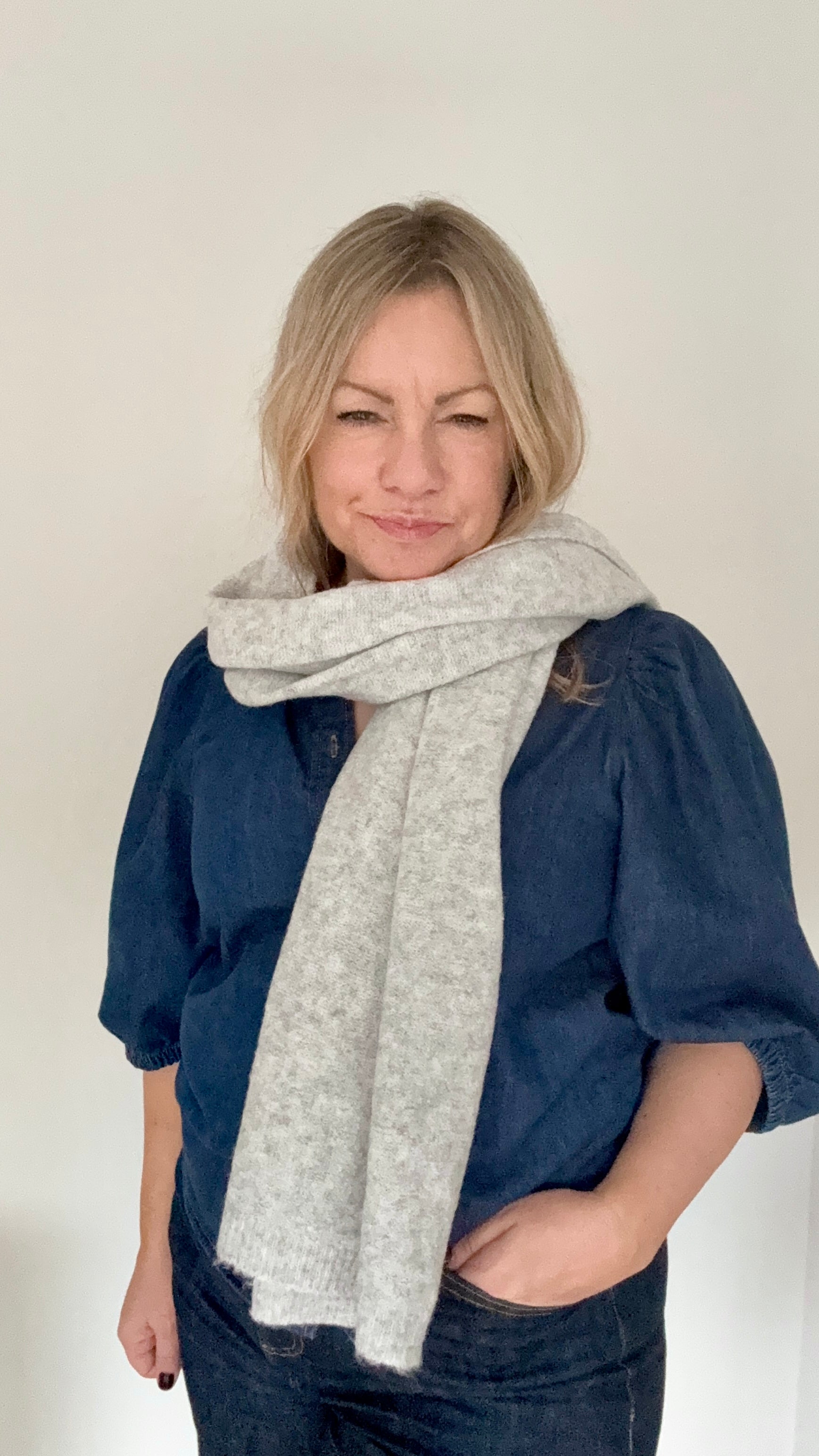 Woman wearing a blue denim shirt and grey knitted blanket scarf