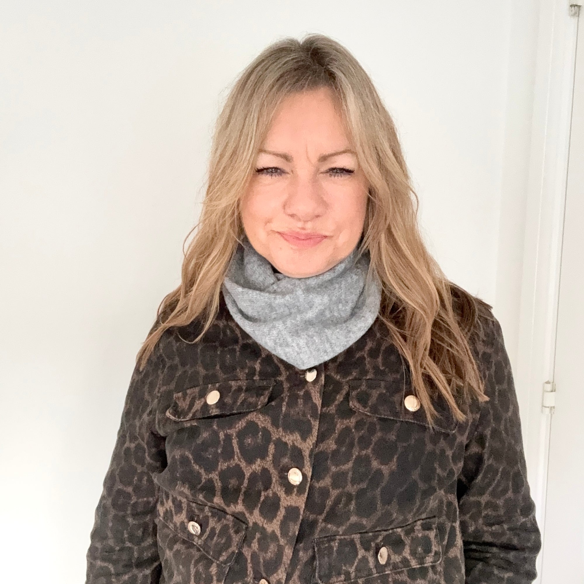Woman wearing a leopard print coat and grey knitted triangle scarf against a white background