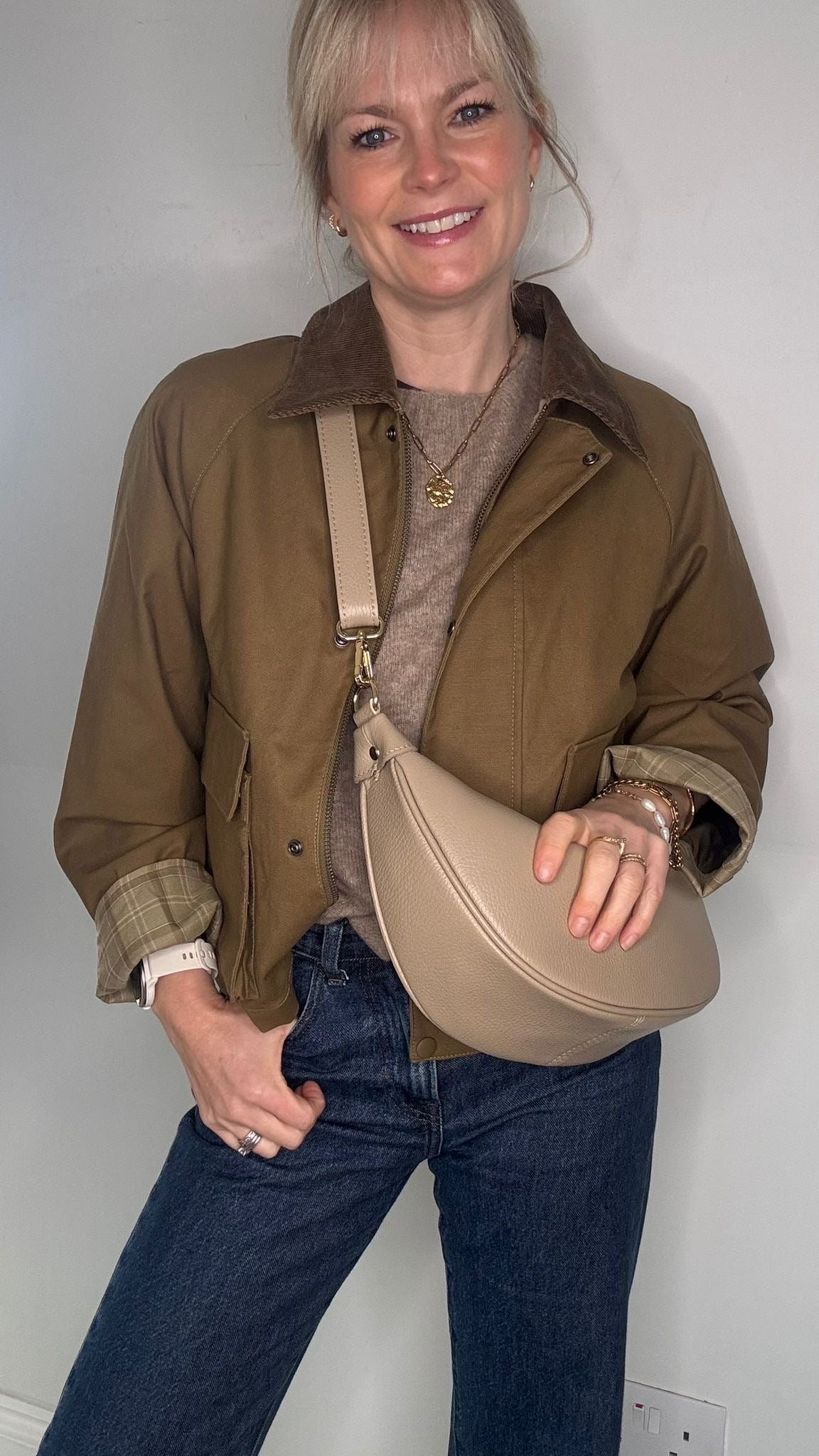 Woman wearing a brown jacket and holding a light taupe bag 