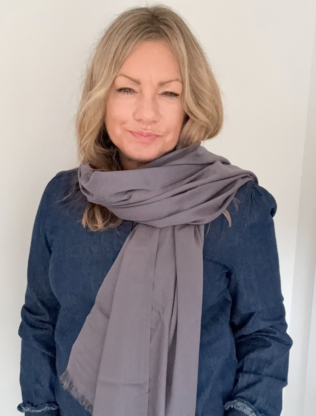 Woman wearing a gray scarf and blue top against a white background