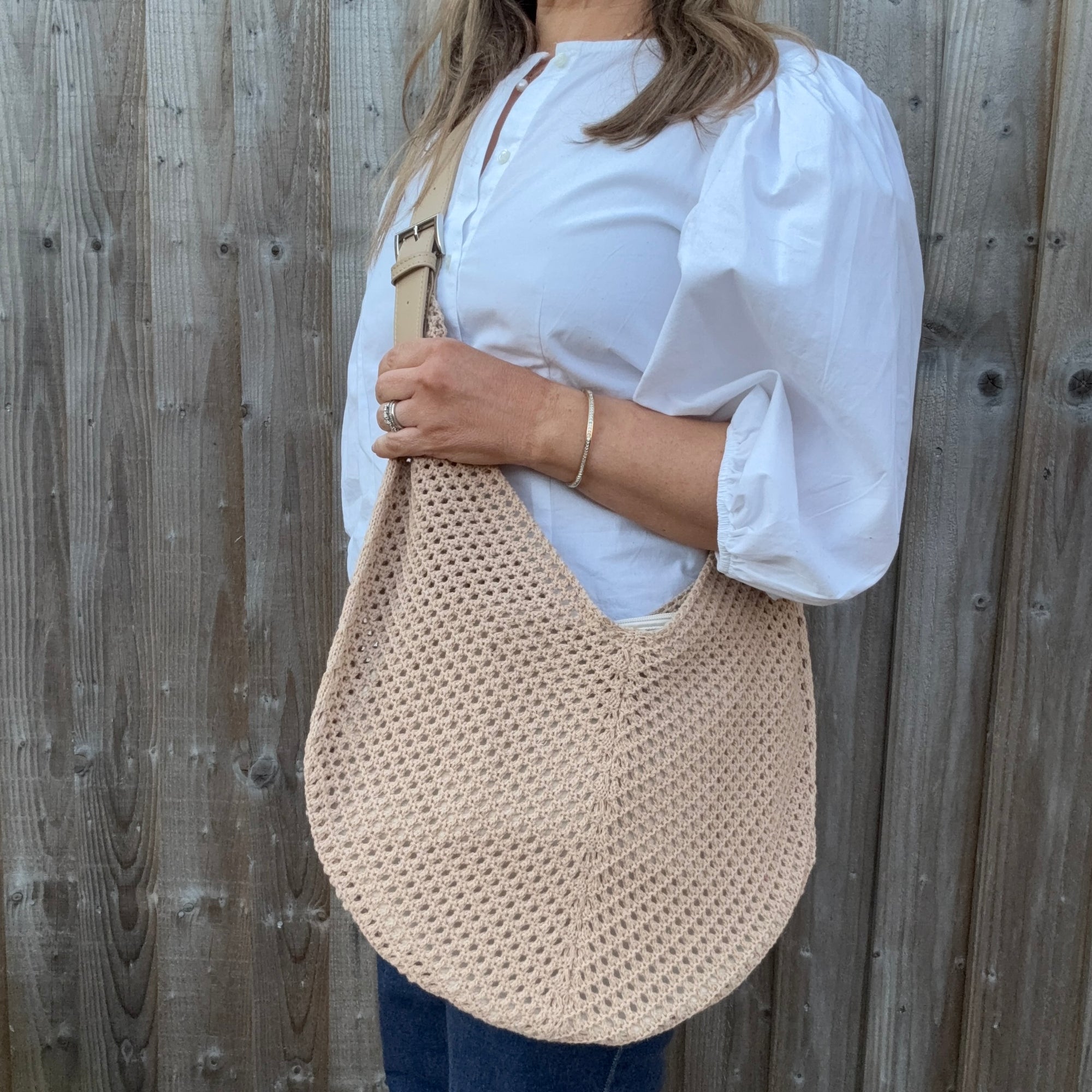 Woman wearing a white shirt and holding a natural woven crossbody handbag. 