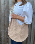 Woman wearing a white shirt and holding a natural woven crossbody handbag. 