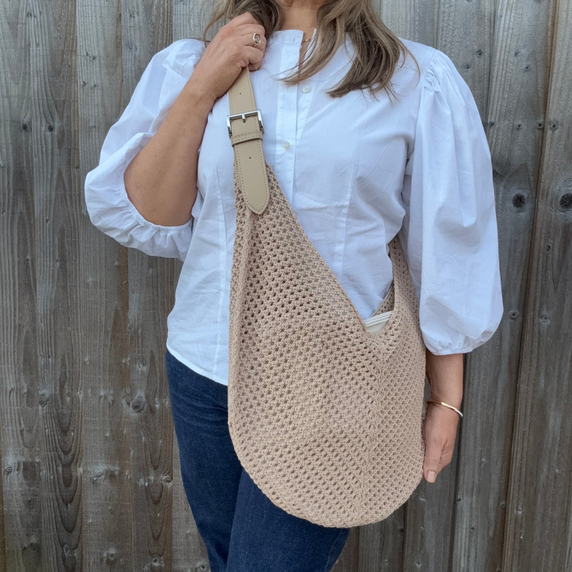 Woman wearing a white shirt and holding a natural woven crossbody handbag. 