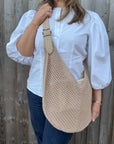 Woman wearing a white shirt and holding a natural woven crossbody handbag. 