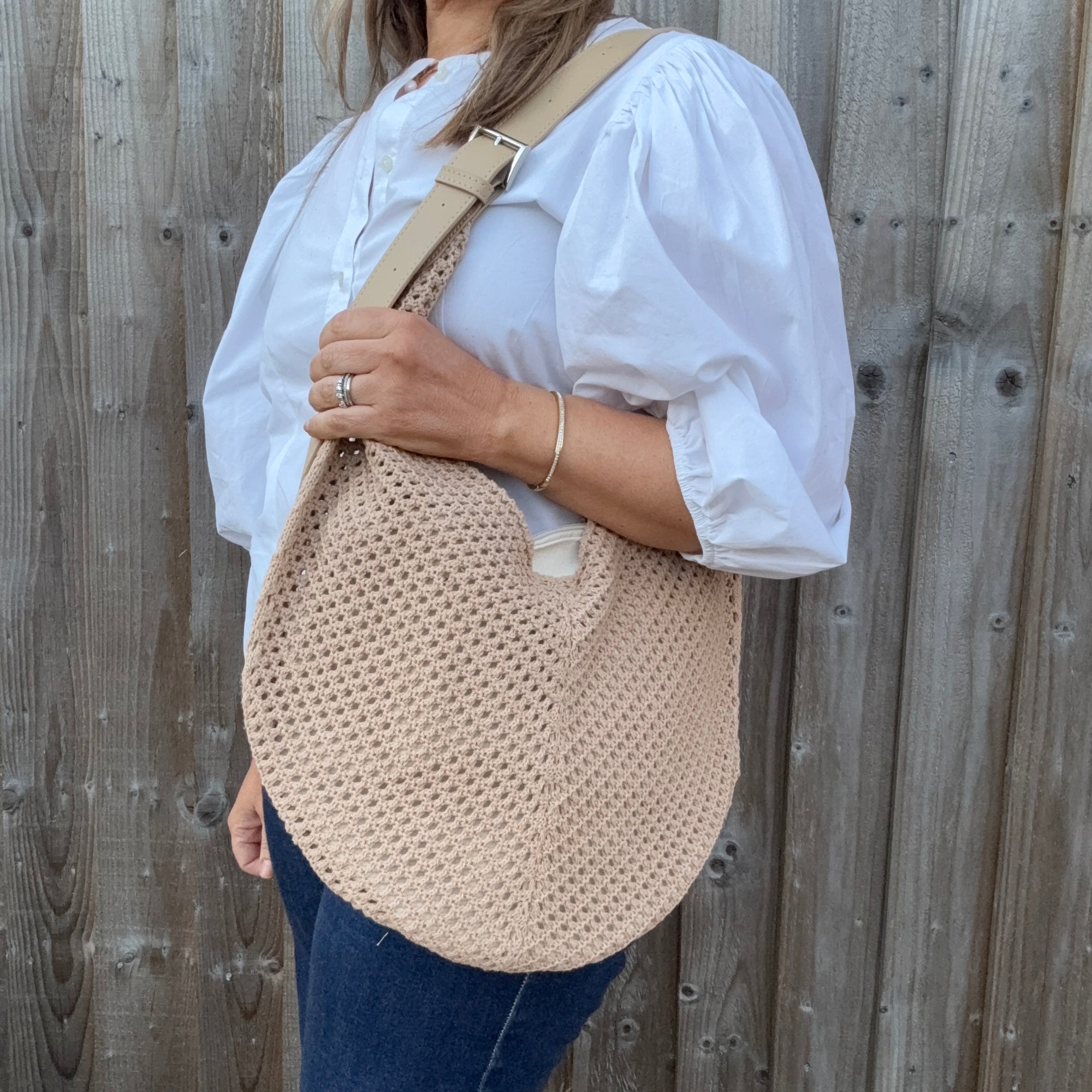 Woman wearing a white shirt and holding a natural woven crossbody handbag. 