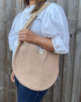 Woman wearing a white shirt and holding a natural woven crossbody handbag. 