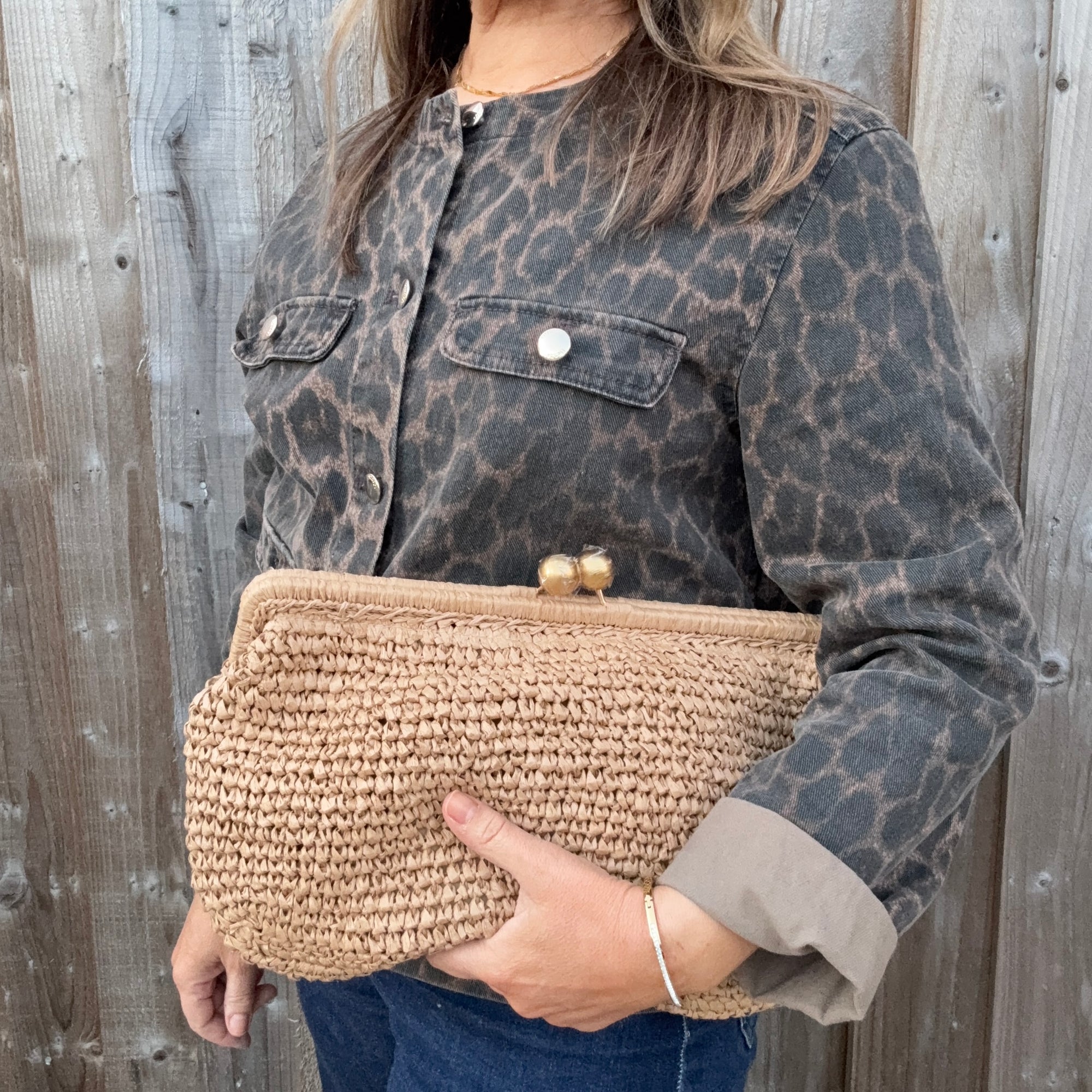 Woman wearing a leopard print jacket, holding a woven clutch.