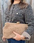 Woman wearing a leopard print jacket, holding a woven clutch.