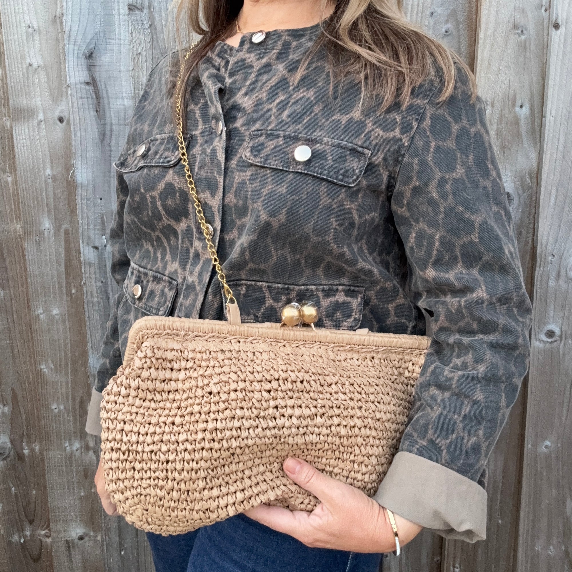 Woman wearing a leopard print jacket, holding a woven clutch with gold strap. 