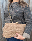 Woman wearing a leopard print jacket, holding a woven clutch with gold strap. 
