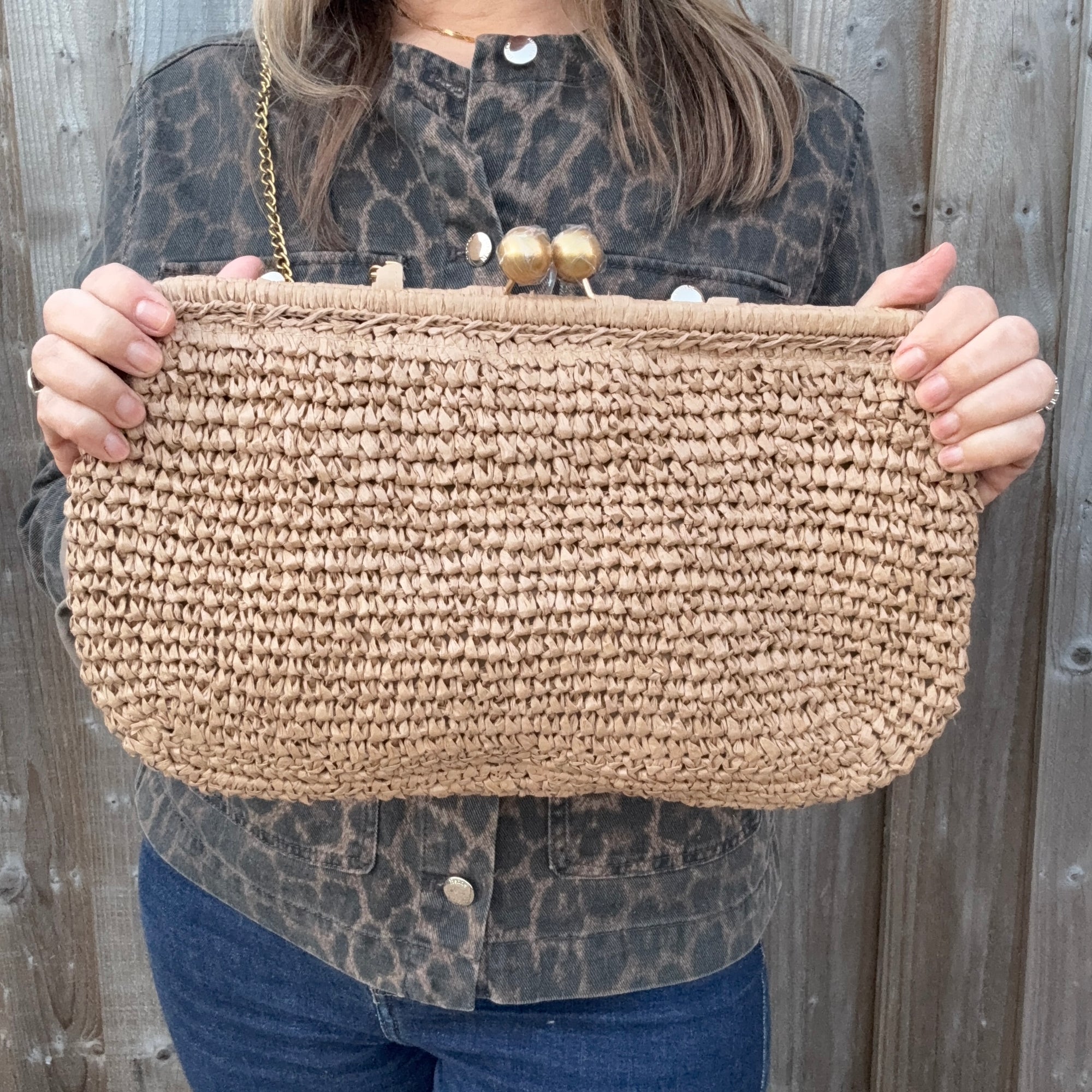 Woman wearing a leopard print jacket, holding a woven clutch with a gold strap and gold clasp. 