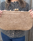 Woman wearing a leopard print jacket, holding a woven clutch with a gold strap and gold clasp. 